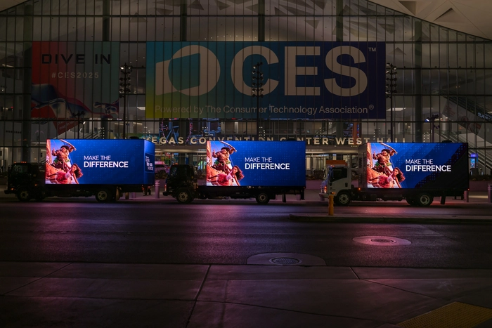 Three LED mobile billboard trucks parked in formation outside CES convention center displaying vivid advertising at night
